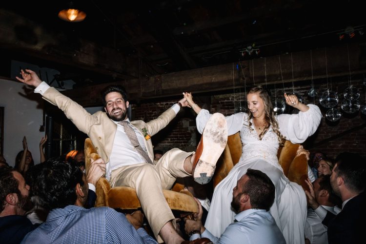 Bride and groom lifted on chairs, celebrating with guests on dance floor