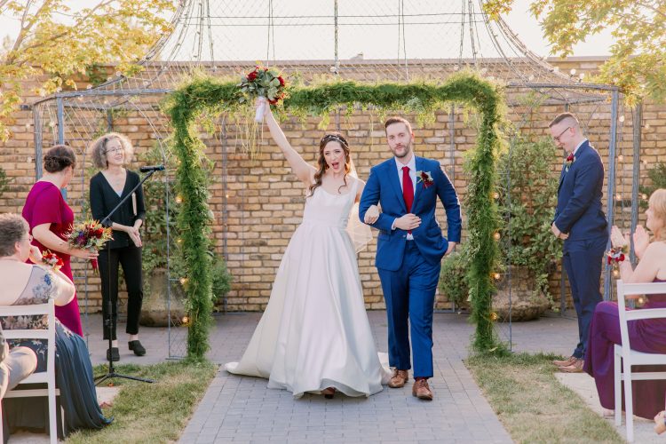 Bride and groom celebrating their exit under a floral arch.