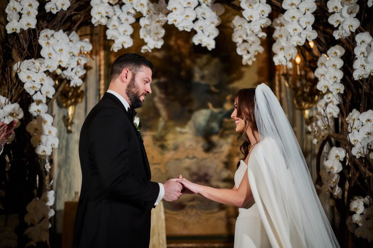 Bride and groom exchanging vows beneath a floral arch.