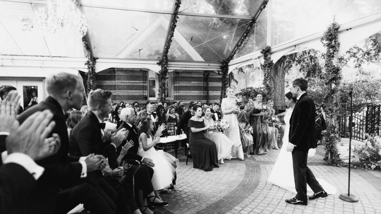 Bride and groom walking into wedding ceremony as guests applaud indoors at Tavern on the Green