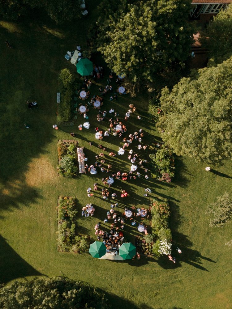 Aerial view of outdoor wedding reception with guests gathered across garden lawn at sunset