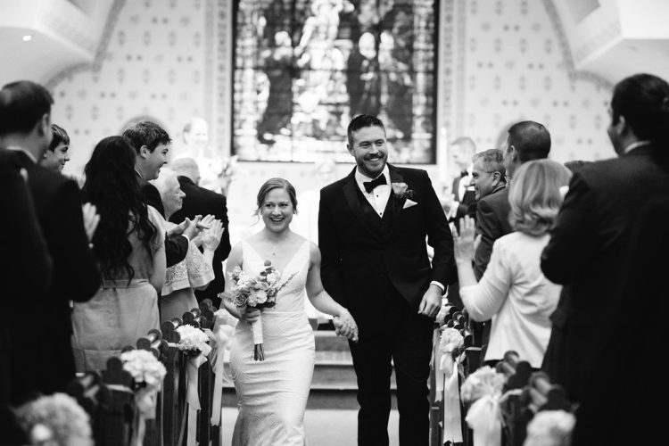 Newly married couple walking down church aisle as guests applaud