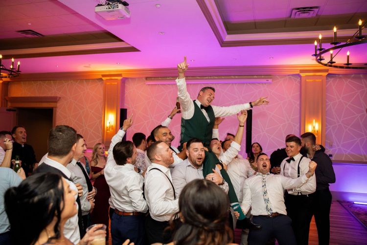 Wedding guest lifted above the dance floor as friends celebrate around him