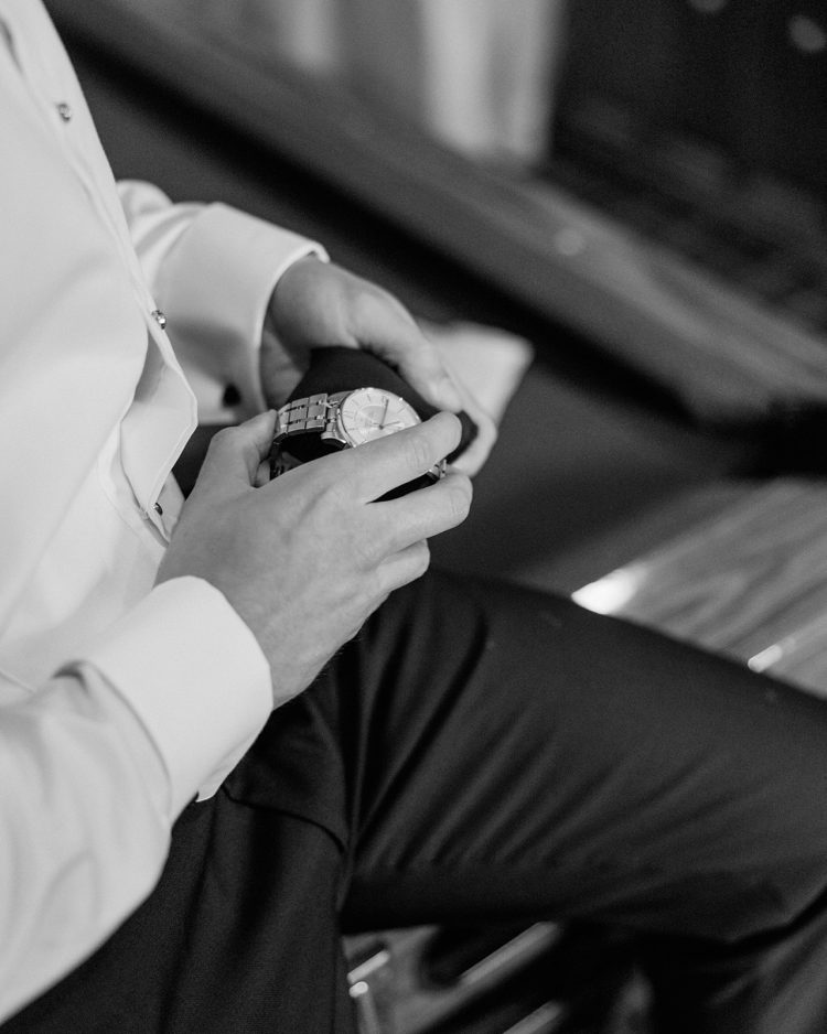 Groom holding wristwatch while getting ready for wedding