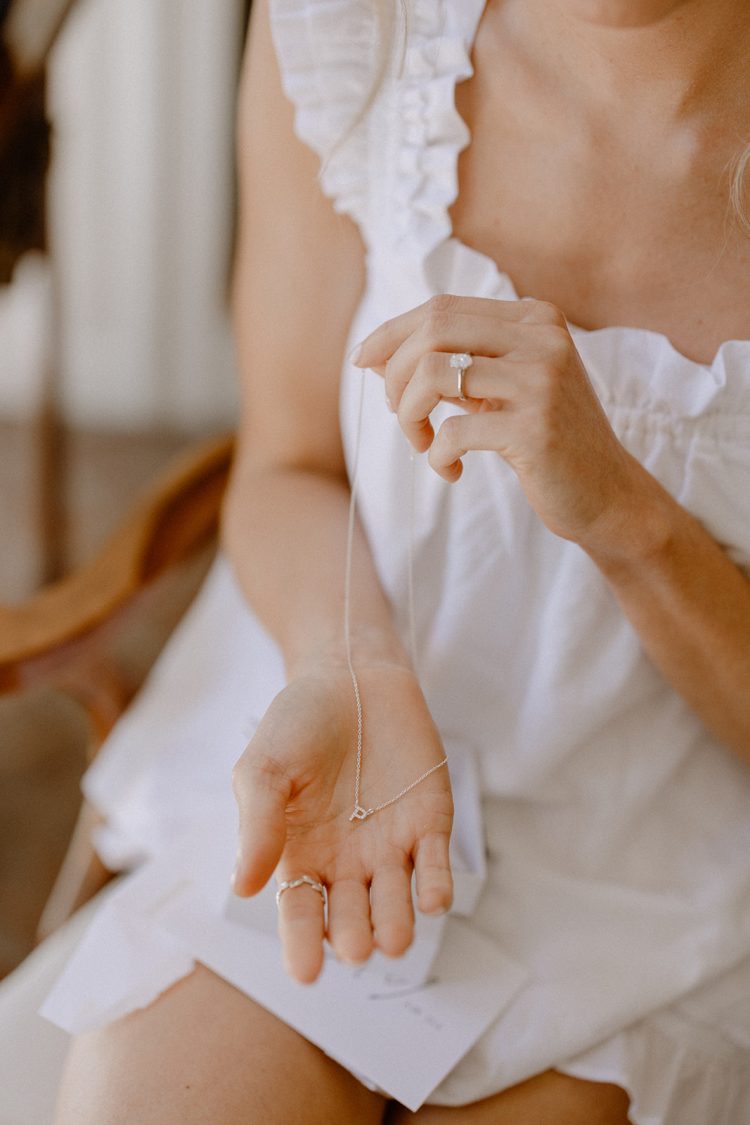 Bride holding delicate necklace while wearing engagement ring