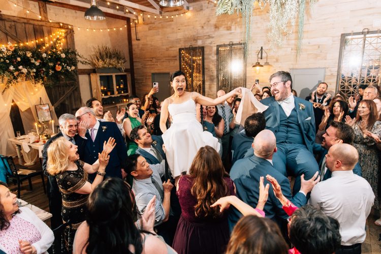Bride and groom lifted on chairs as wedding guests celebrate around them