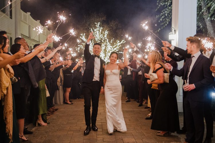 Bride and groom walking through a sparkler exit surrounded by wedding guests