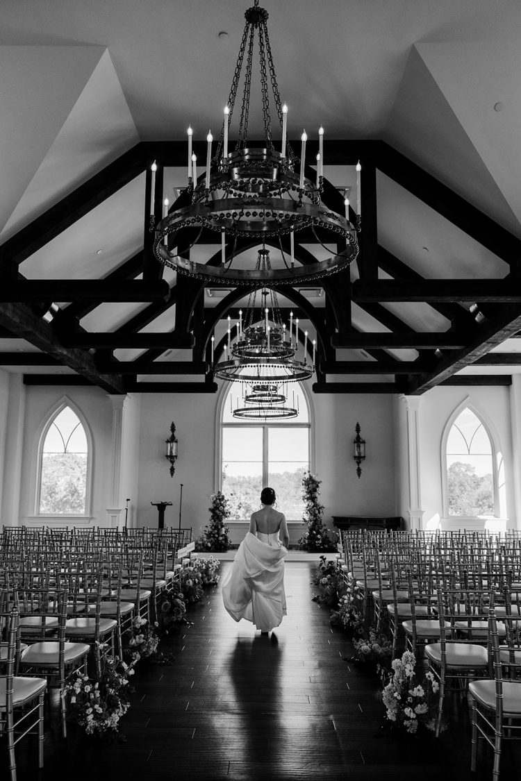 Bride walking down the aisle inside an elegant chapel with exposed wooden beams and chandeliers at The Park Savoy Estate
