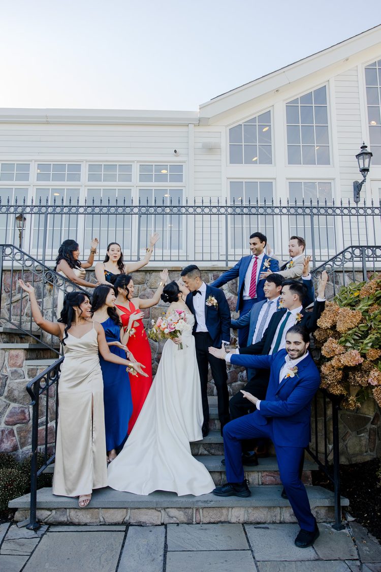 Bride and groom kissing on outdoor steps surrounded by their wedding party at The Park Savoy Estate