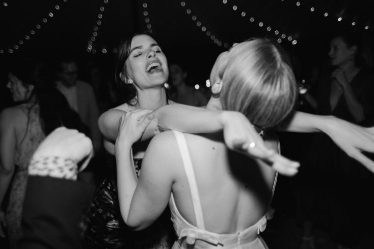 Wedding guests embracing on crowded dance floor beneath string lights